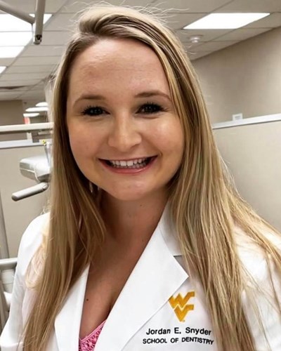 Jordan is seen smiling in a dental facility while wearing a white WVU School of Dentistry lab coat