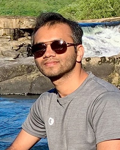 Habibul is wearing sunglasses as he sits on the rocky shore of a stream.