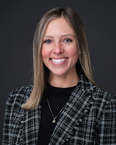 Haley smiles for the camera, wearing a black blouse with a black sportcoat with white patterned stitching, and a necklace.