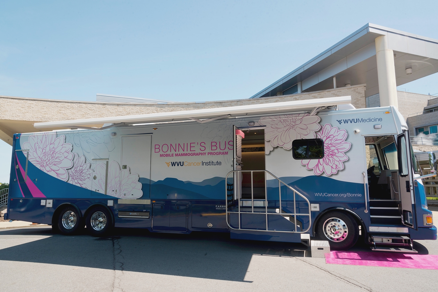 Bonnie's Bus, a mobile mammography bus from WVU Medicine with floral graphics, parked outside building and with a pink mat at the entrance.