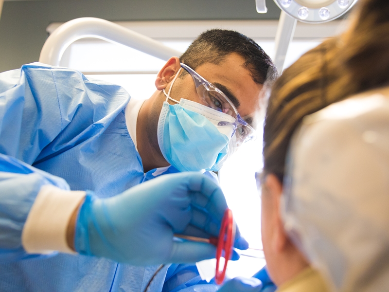 A student with the School of Dentistry examines a patients mouth during a clinical training session.
