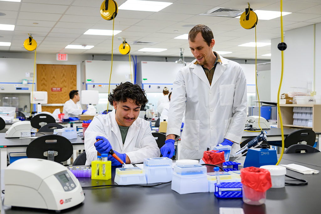 Laboratory personel performsing lab work at a table with different equipment.