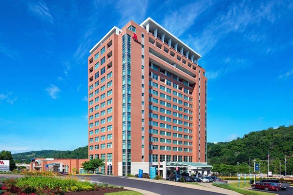 Exterior of the Marriott and Morgantown Event Center, a high-rise red brick building situated in a hilly landscape with a covered entrance and parking.