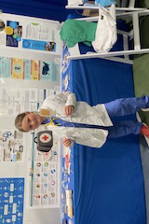 A person dressed in a white coat and scrubs by a display table and poster at the Mon county fair.