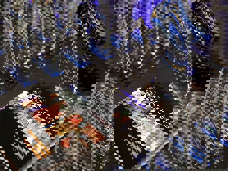 A collection of crystal awards and a medical textbook arranged on a dark tabletop. In the foreground is a book titled "Atlas of Surgical Techniques in Trauma." Behind it, several glass trophies are visible. A blue and black glass sculpture stands in the background.